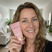 Vrouw van rond de 50 houdt het Velveux Bio Collageen Masker bij haar wang in de woonkamer